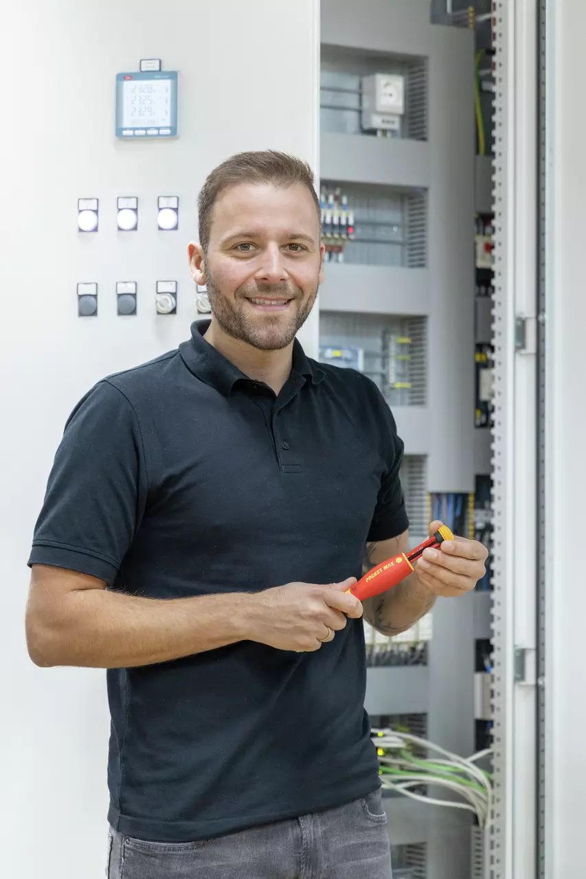 Person holding a red electric screwdriver in front of an open electrical panel.