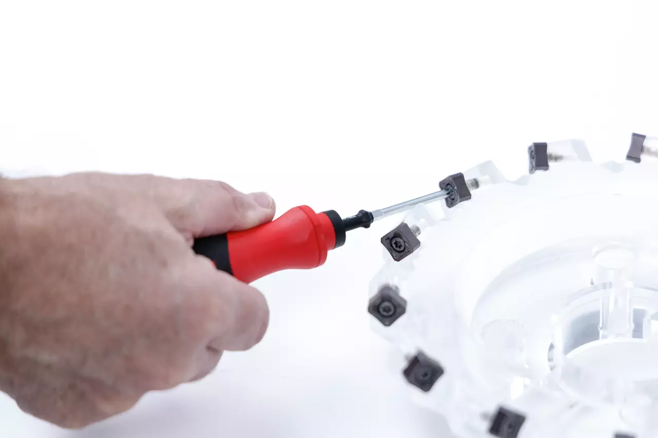 Person using red-handled screwdriver to adjust a round tool with inserts.