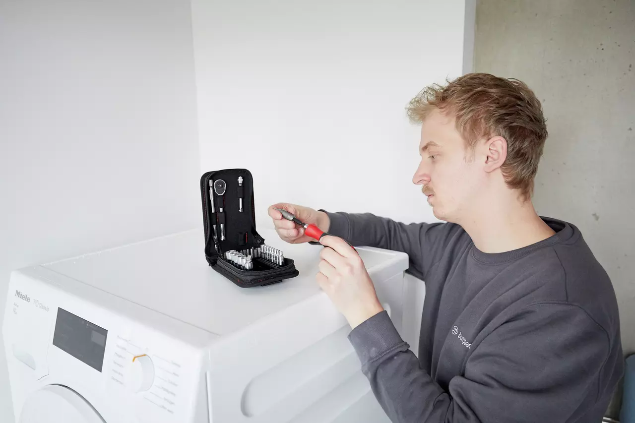 A person using a screwdriver set on top of a washing machine.