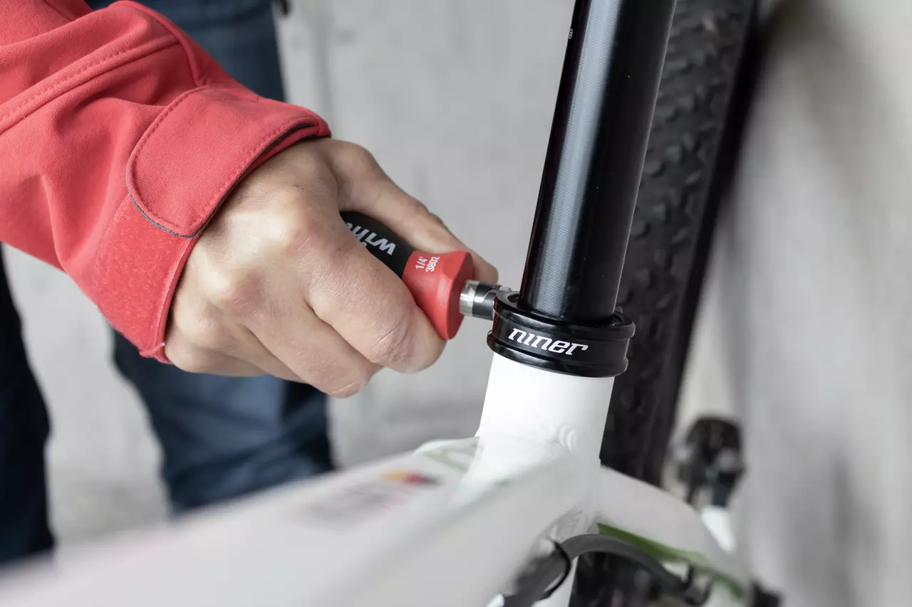 Iemand gebruikt een kleine schroevendraaier om een fietszadelklem aan te passen.