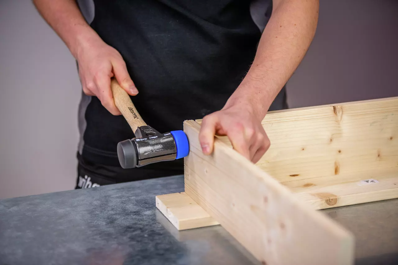 Person using a mallet with a wooden handle on a wooden structure.