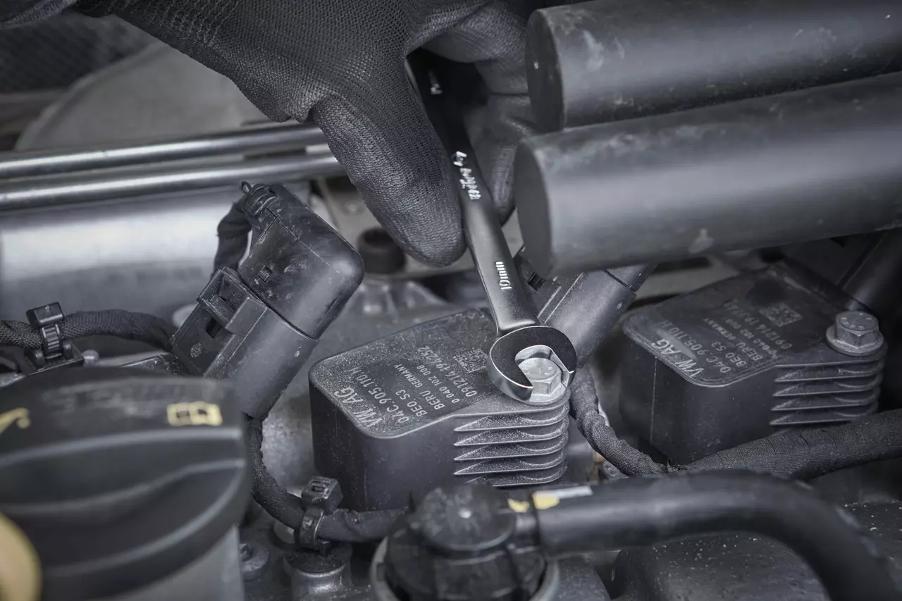 A person uses a ratchet wrench on a bolt in a car engine area.