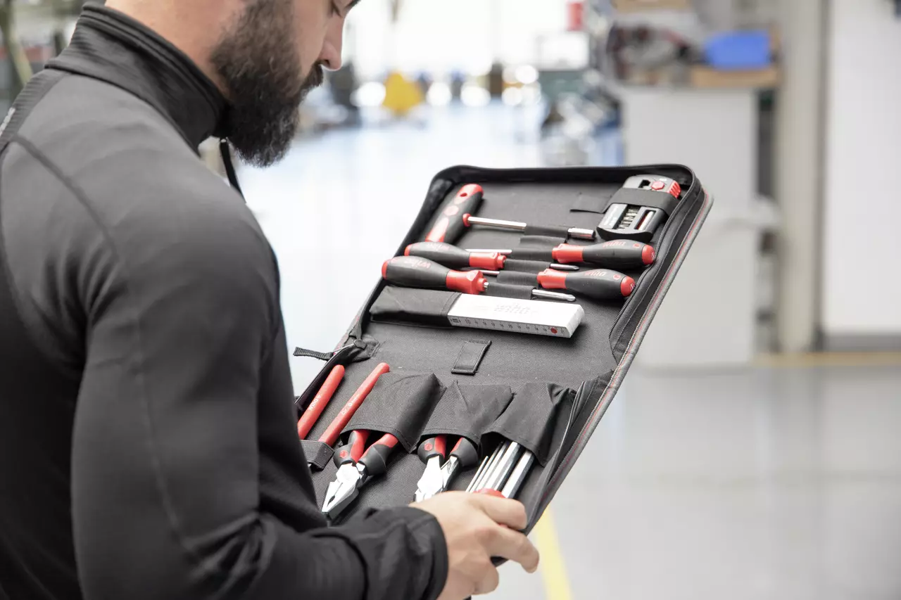 A person holding a tool set with various hand tools in a black case.