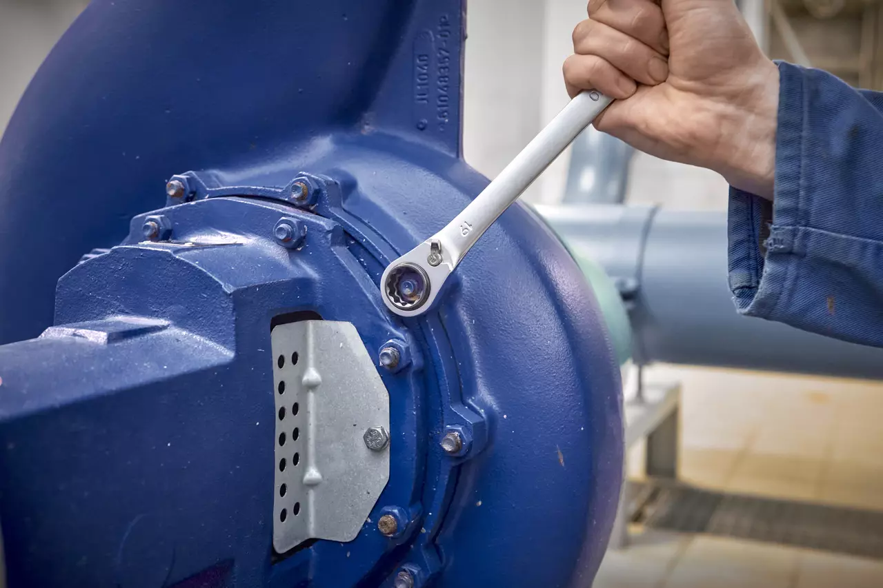Une personne utilise une clé à cliquet sur une grande machine industrielle bleue.