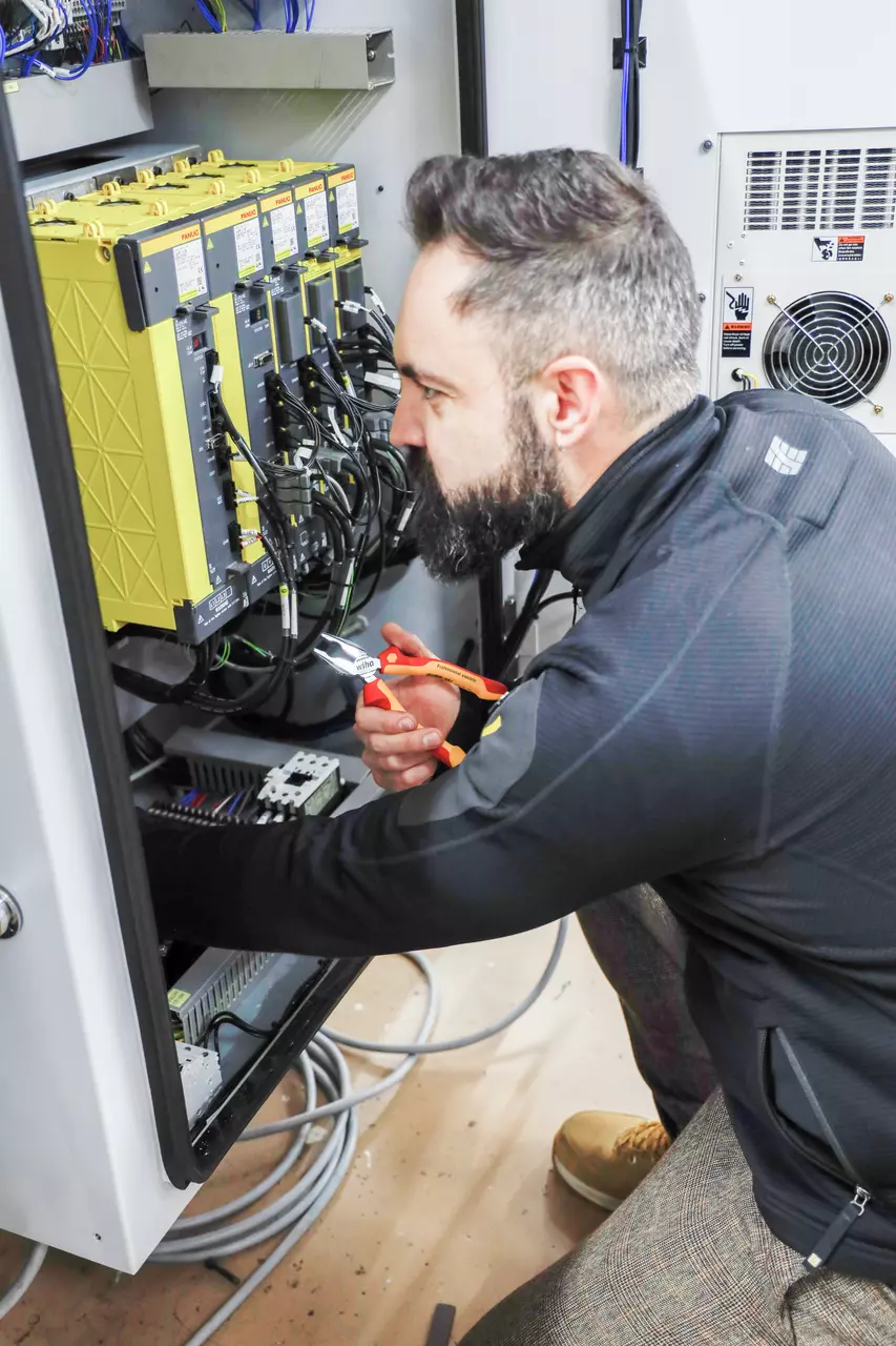 Person working on electrical panel with combination pliers.