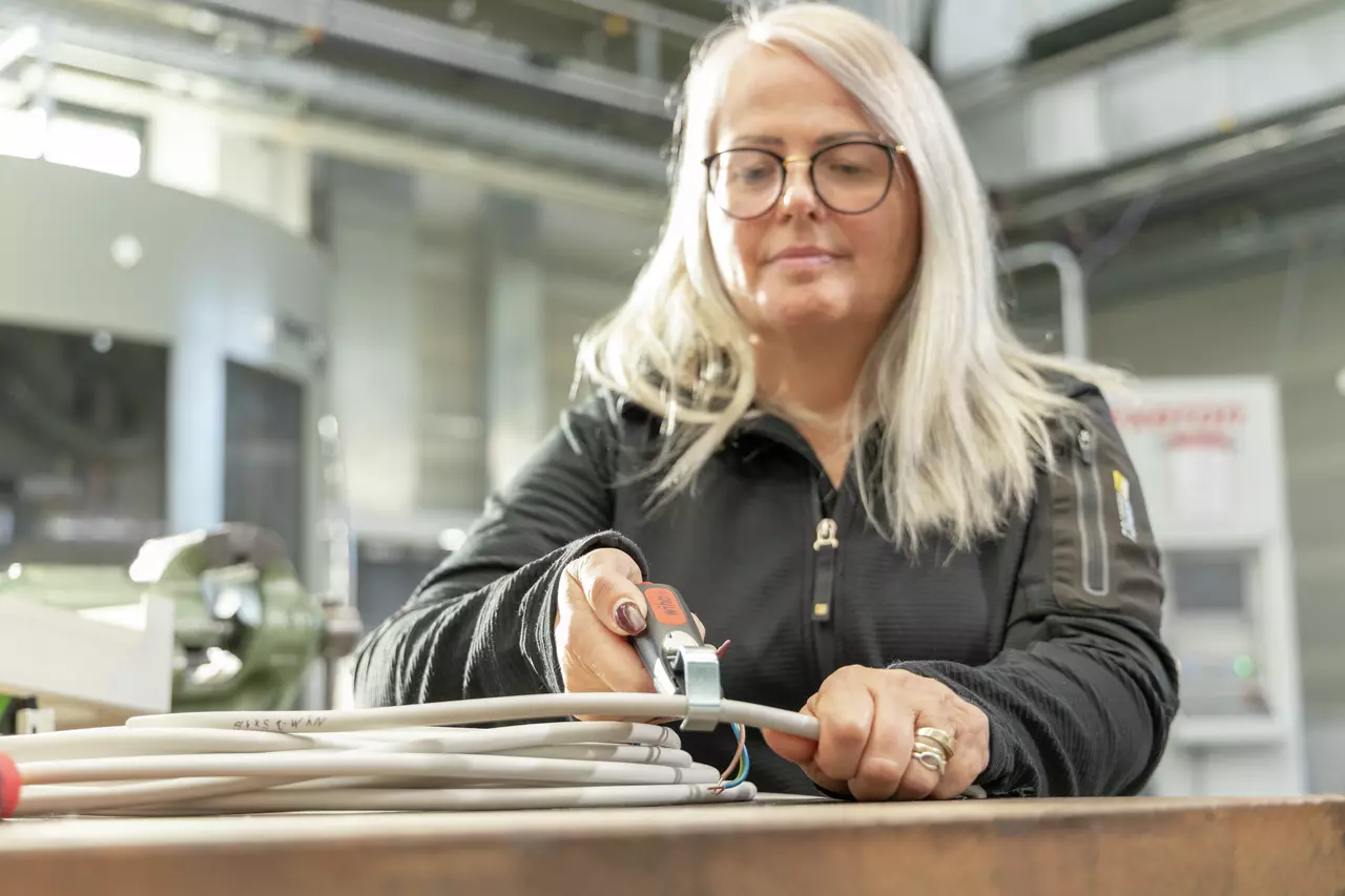A person using a cable stripping tool on a white cable in an industrial setting.