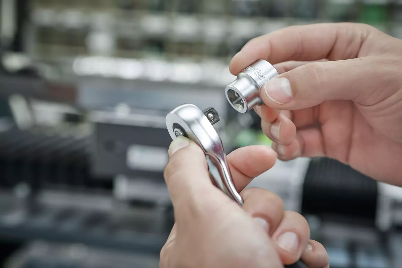 A person holding a ratchet wrench and a socket in their hands.