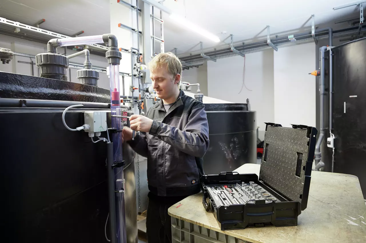A person working on pipes in a workshop with an open socket set case nearby.
