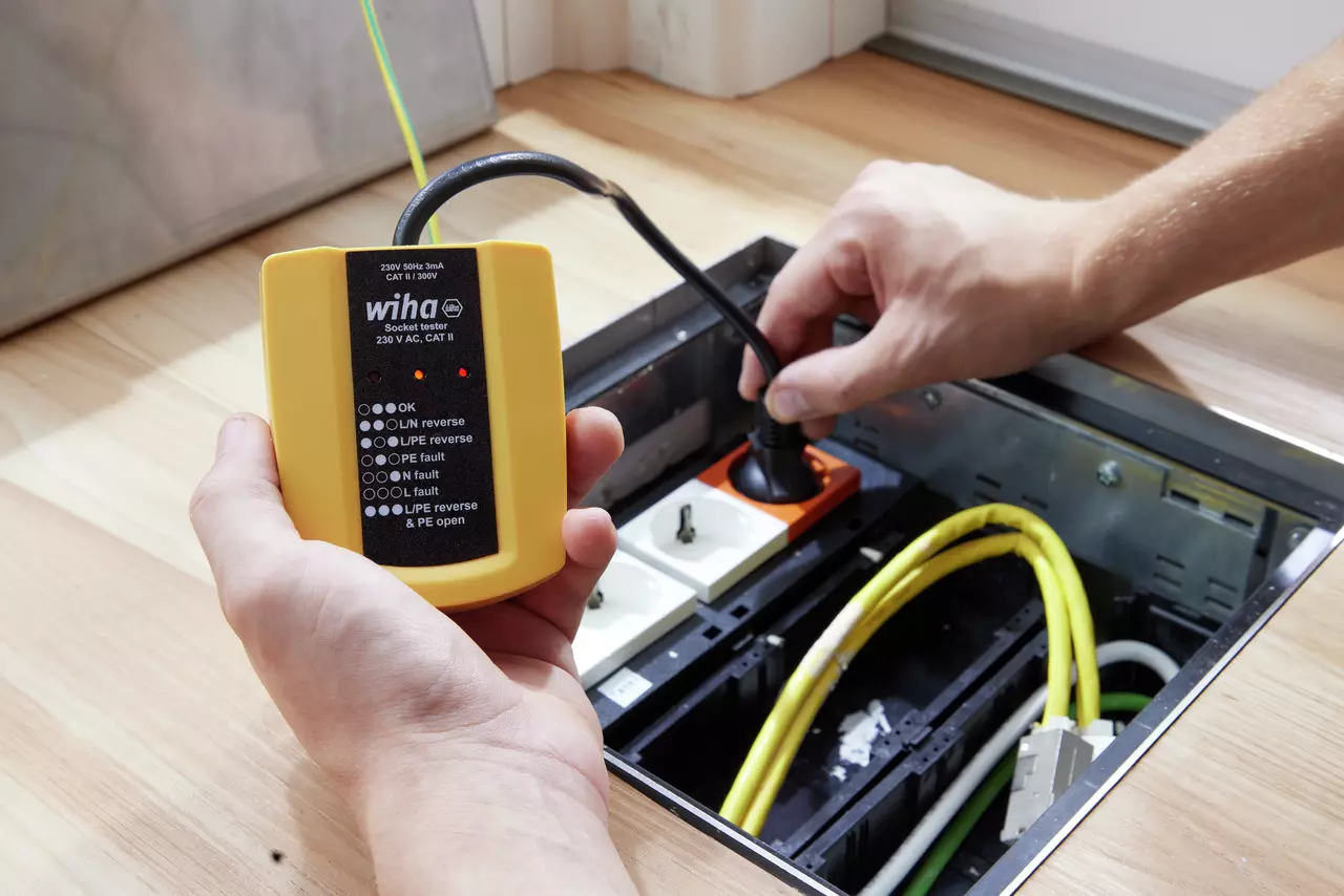 A person using a yellow socket tester to check an electrical outlet in a floor box.