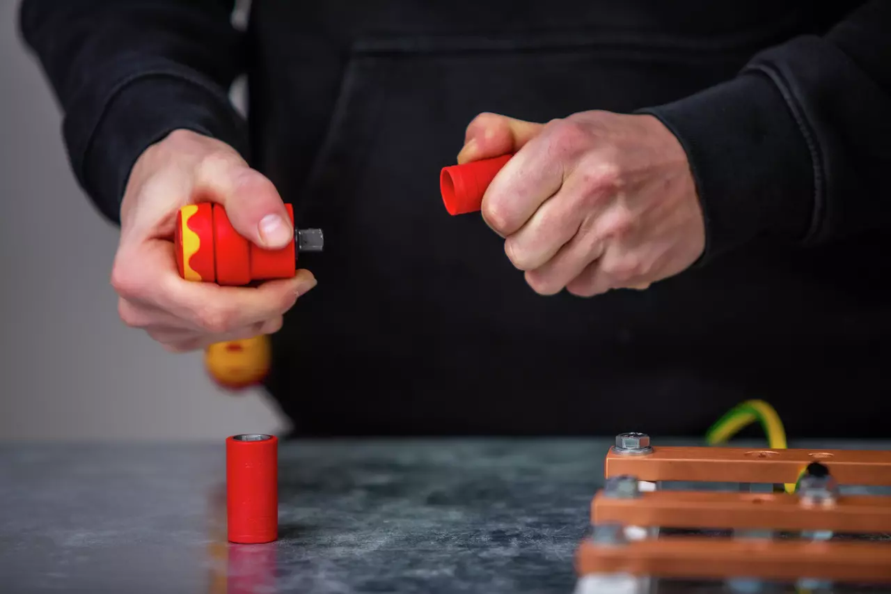A person holding a red and yellow tool, preparing to connect or disconnect parts on a table.