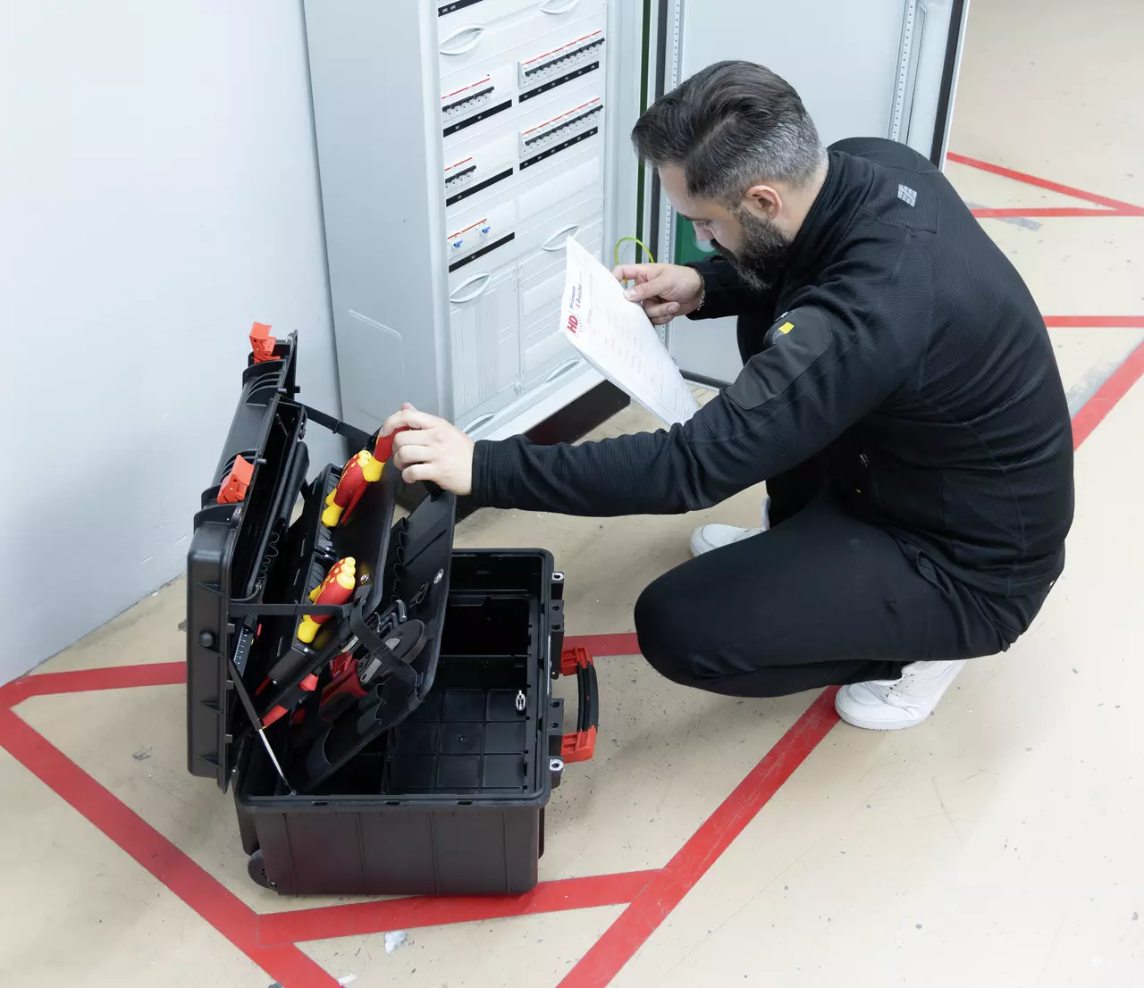 A person kneels in front of an open toolbox next to an electrical cabinet.