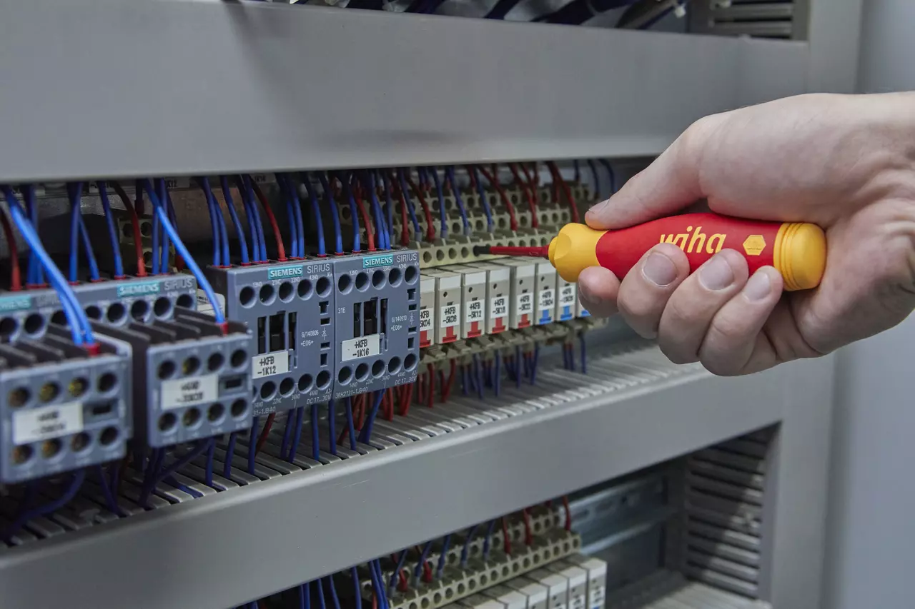 Person using an electric screwdriver on a circuit breaker panel.