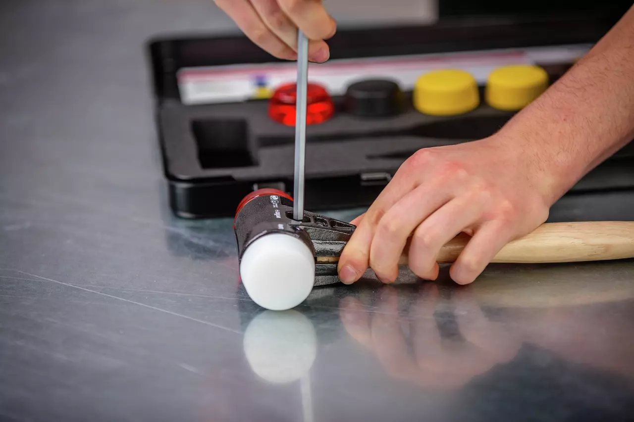 A person assembling a mallet with white rubber heads using a tool, with a tool case in the background.