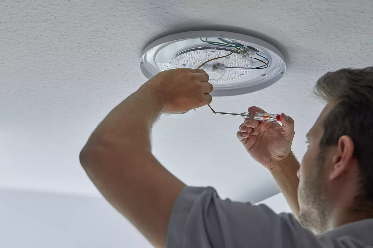 Person using voltage tester on ceiling light wires.