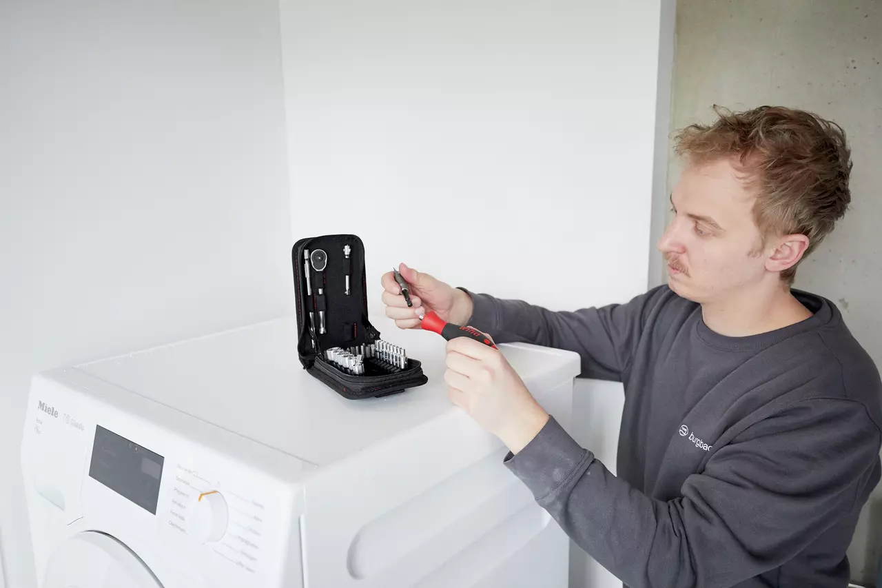 Person using a screwdriver set on top of a washing machine.