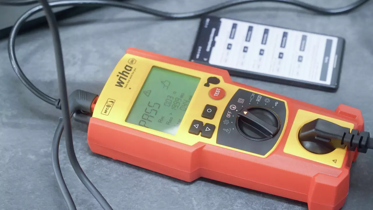 Elektrisk testapparat med digital skærm, rød og gul kabinet, forbundet med sort kabel.