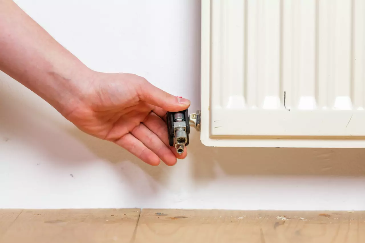 A hand using a tool to adjust a radiator valve