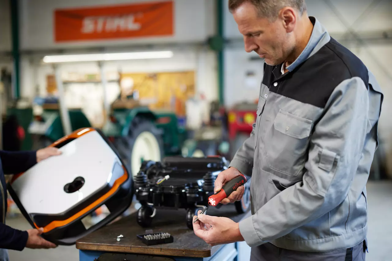 Two people working in a workshop with an electric screwdriver and a device cover.