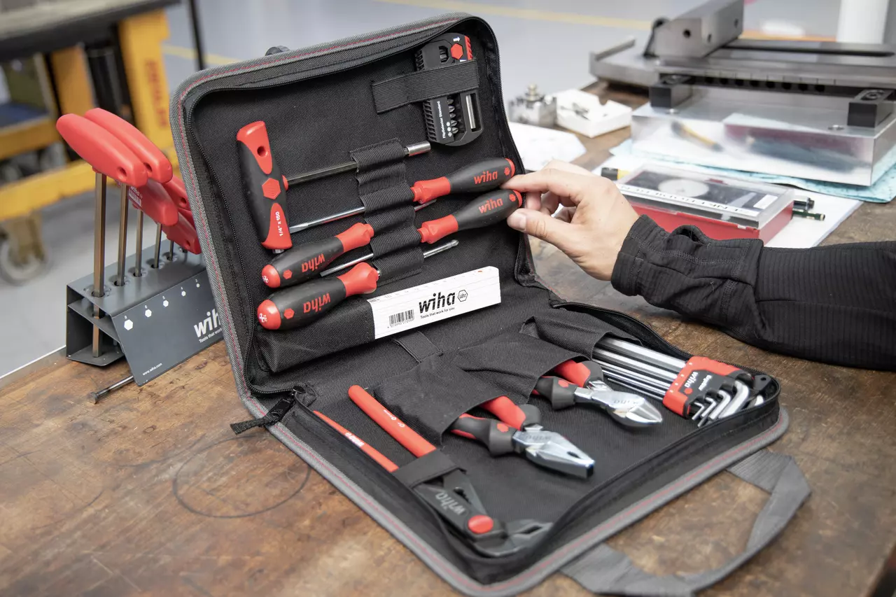 A person handles a tool set in a black case with red-handled screwdrivers, pliers, and hex keys.