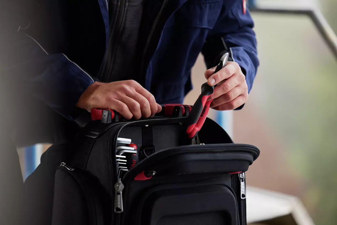 Person taking a tool from a black tool bag.