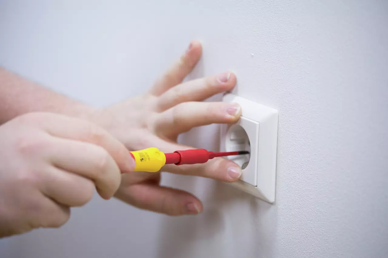 Person using a red and yellow screwdriver on a wall socket