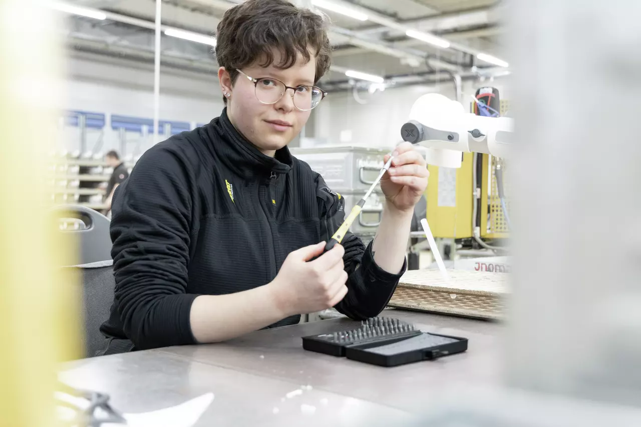 A person holding a screwdriver, sitting at a table in a workshop.