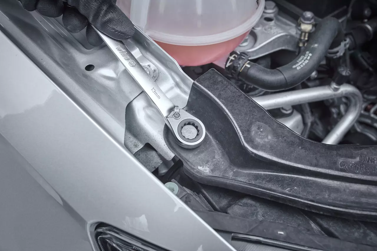 Person using a ratchet wrench on a car engine