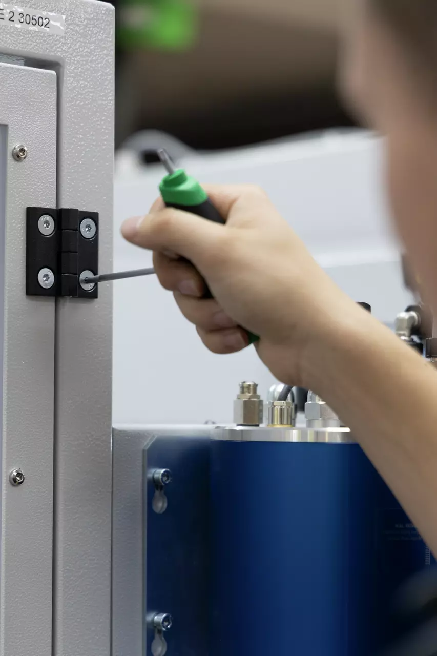 Person using a green-handled tool to adjust a hinge on a metal panel.