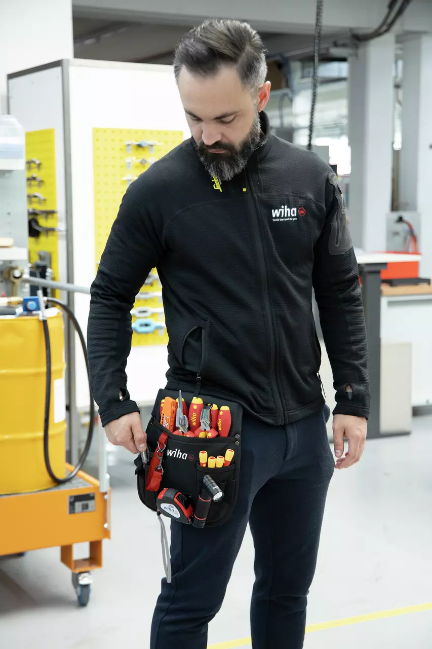 A person wearing a tool belt with various tools in a workshop setting.