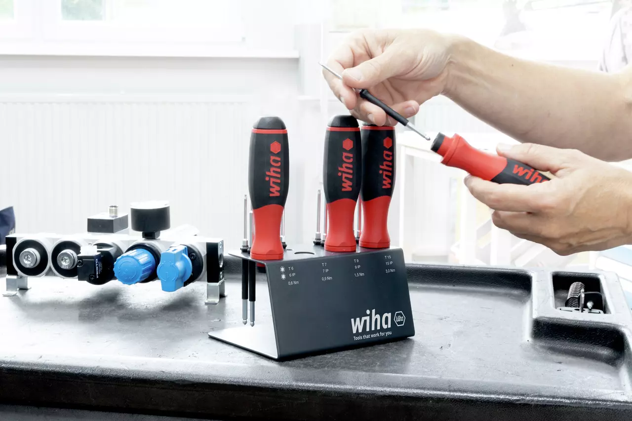 Person using a red and black screwdriver set with a stand on a workbench.