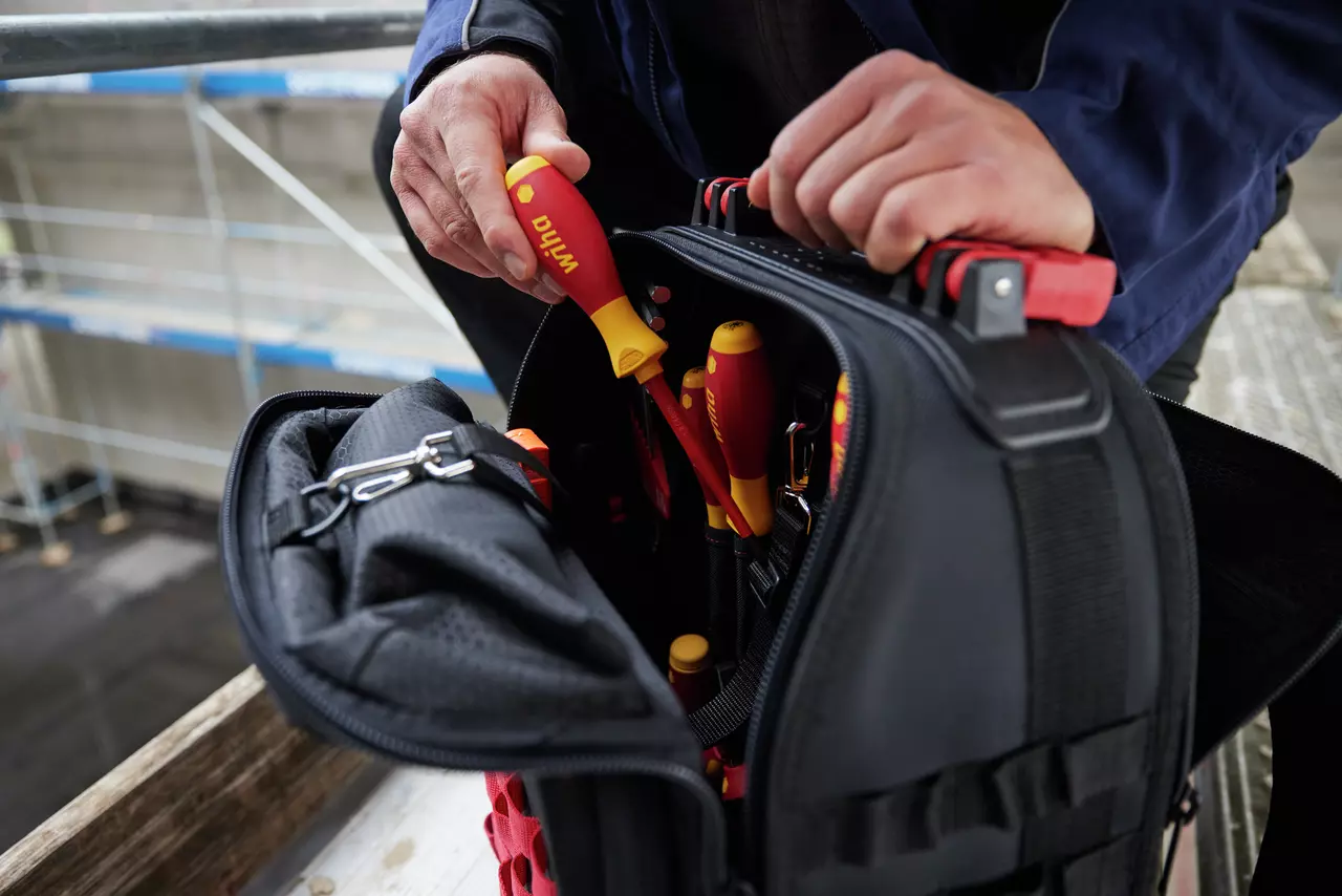 Person placing a screwdriver into a black tool bag with red and yellow handles visible.