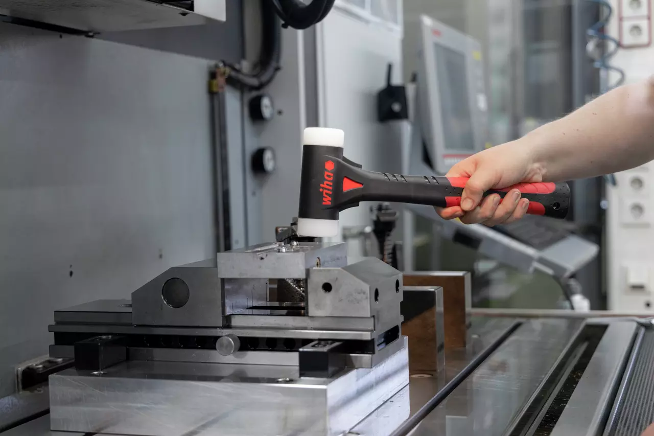 Eine Person benutzt einen schwarz-roten Schonhammer auf einem Metall-Schraubstock in einer Werkstatt.