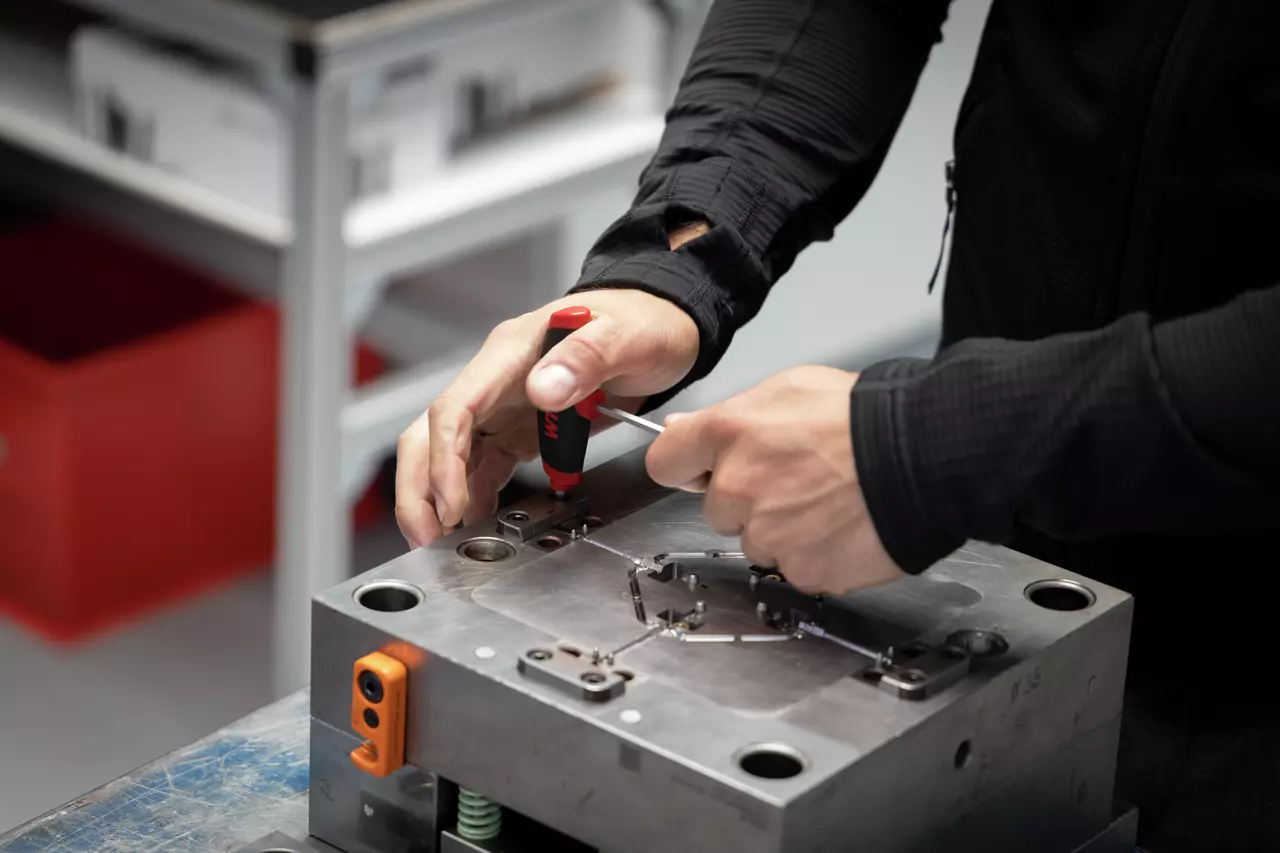 A person using a red-handled screwdriver on a metal mechanical part.