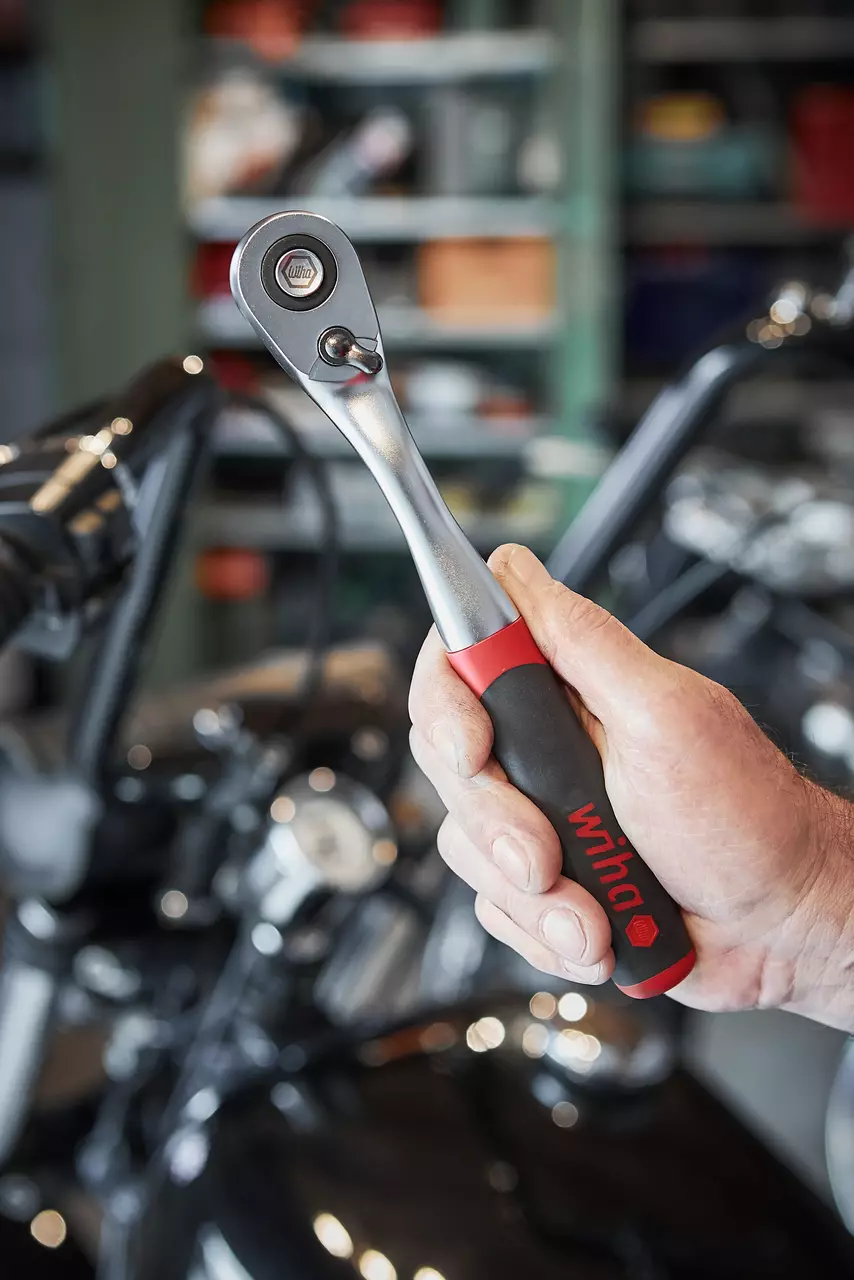 A person holding a reversible ratchet with a black and red handle in a workshop.