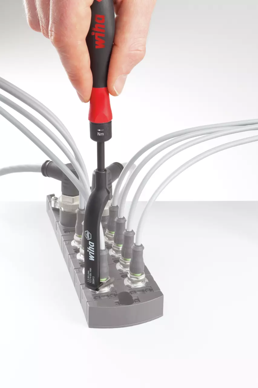 A hand using a torque screwdriver on a cable terminal block with multiple grey cables connected.