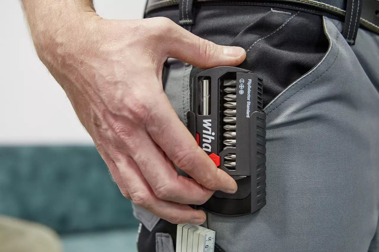 Hand holding a bit set in a black case clipped to a gray work pant pocket.