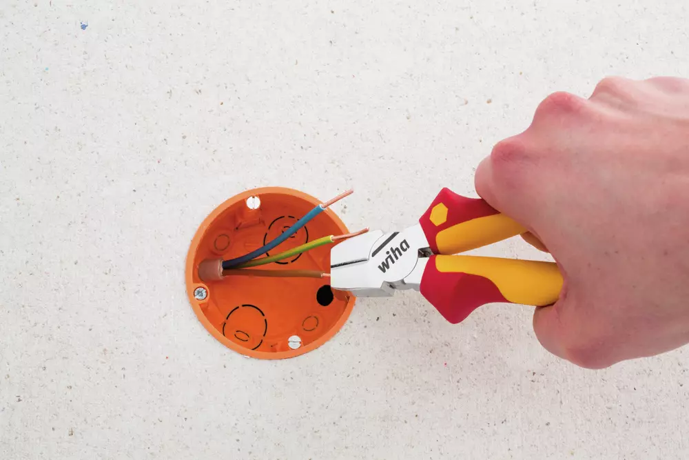 Hand using pliers to strip wires in an orange electrical box