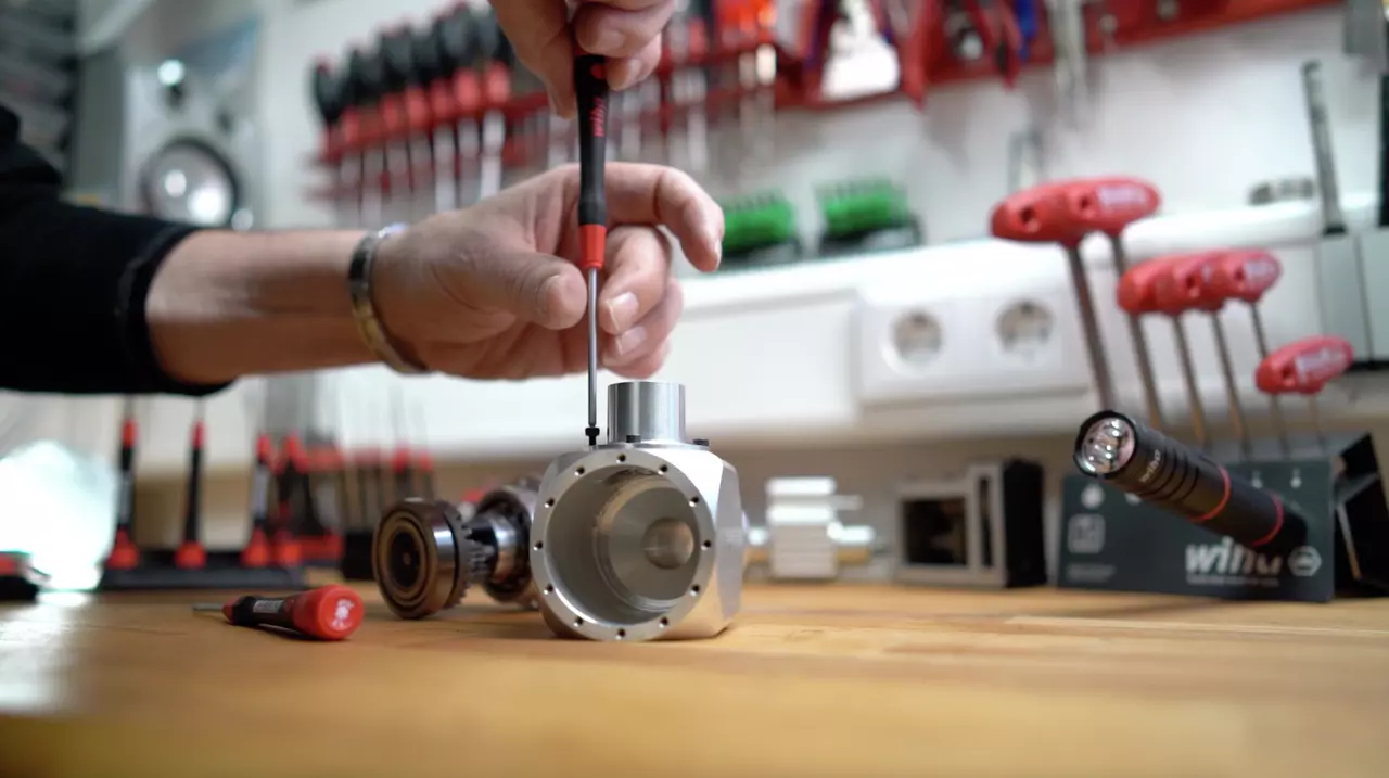 Person using a precision screwdriver on a metal part on a workbench with tools in the background.