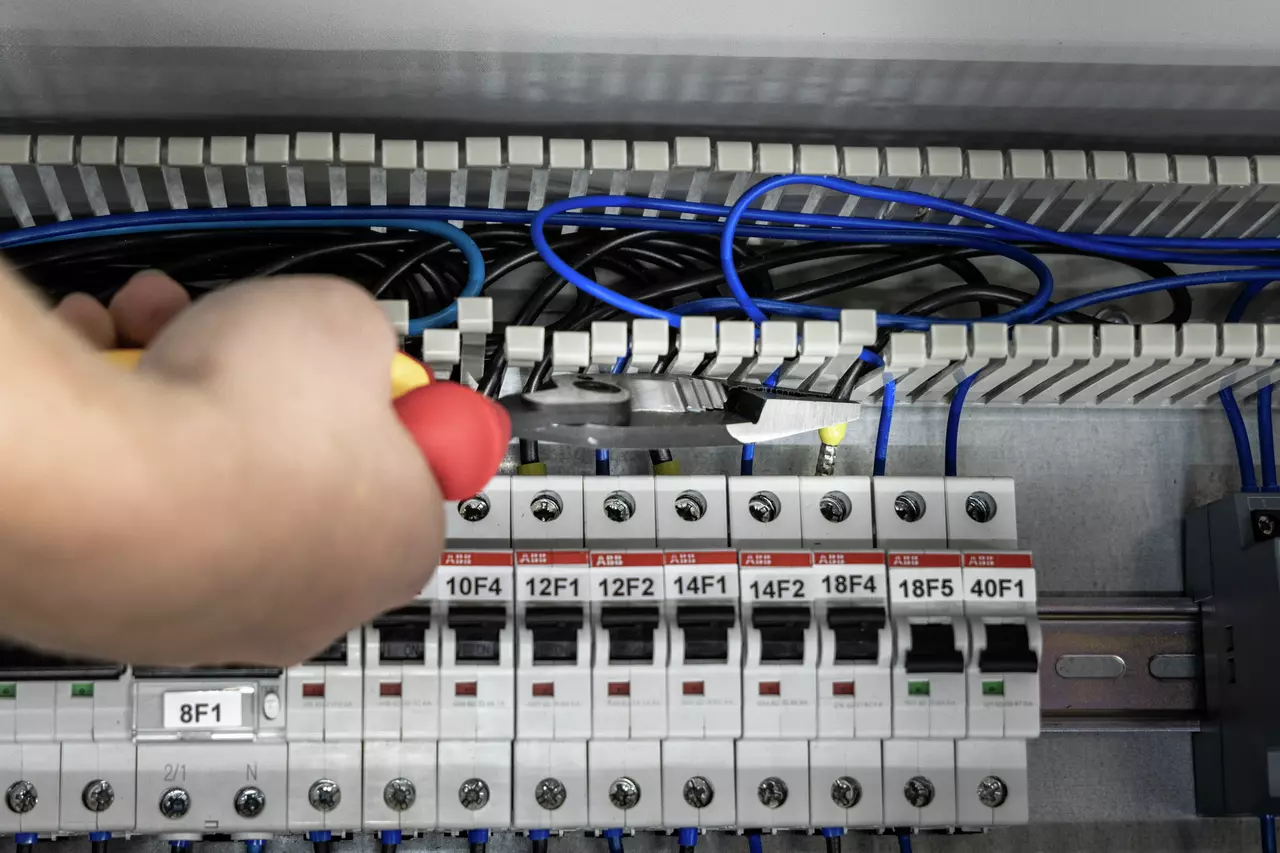 Persoon gebruikt een tang op een elektrisch paneel met blauwe draden en schakelaars.