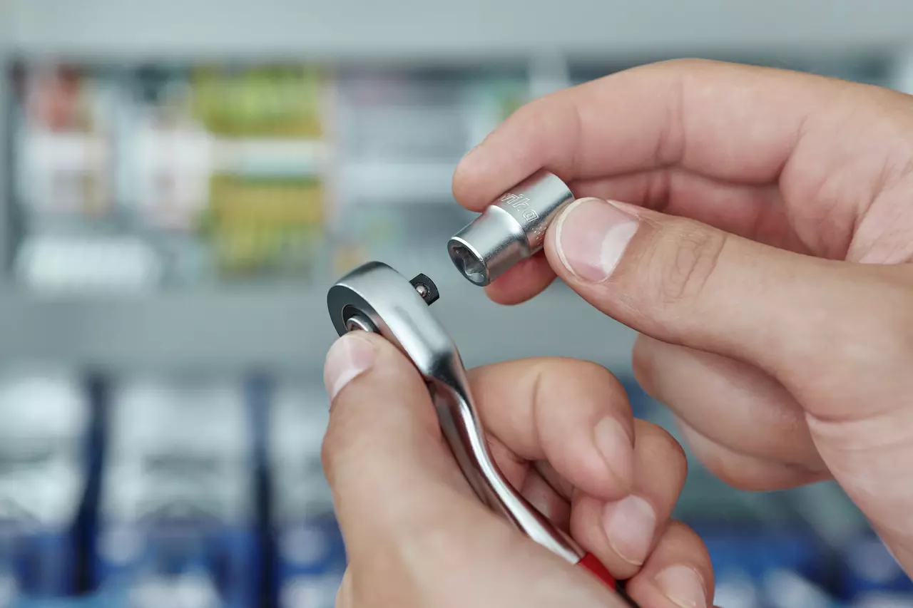 Hands holding a reversible ratchet and a socket, preparing to attach them.