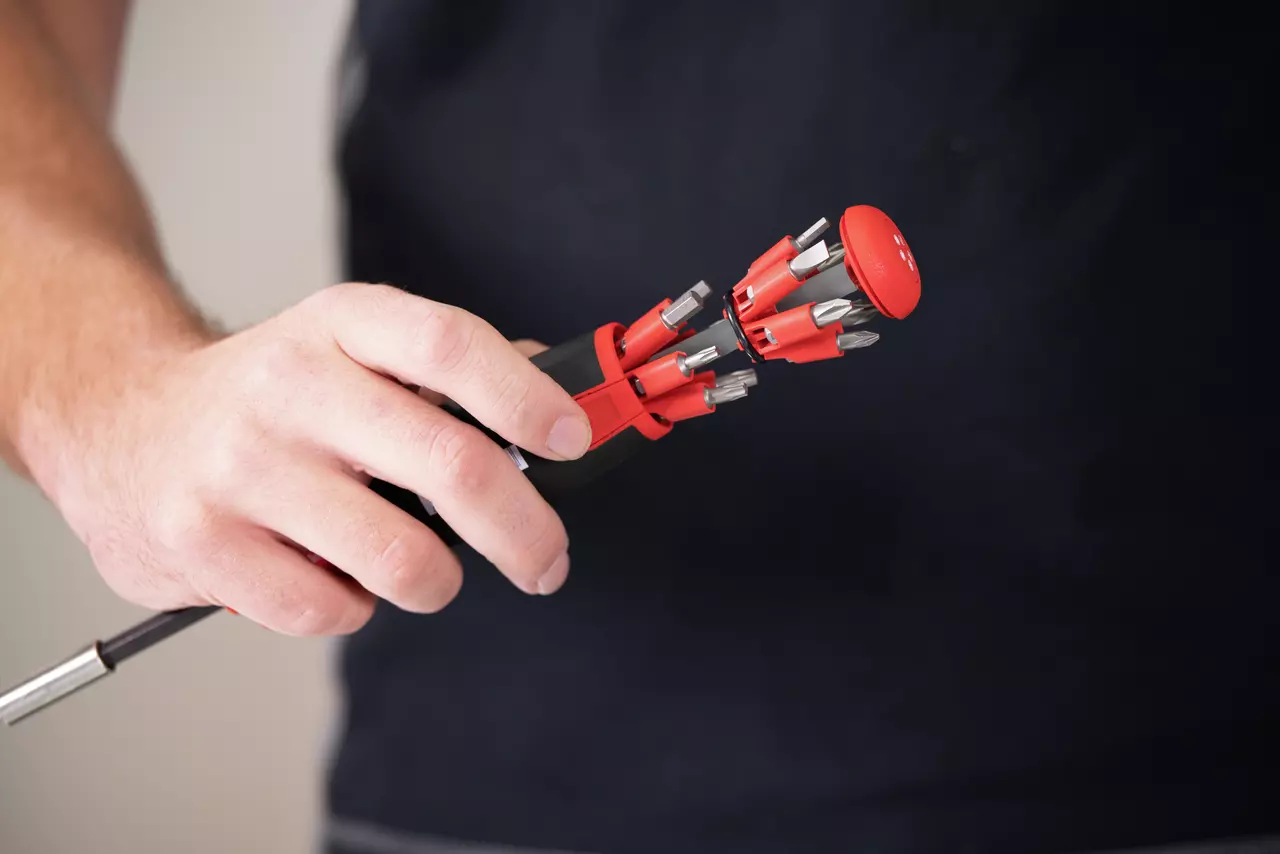 A person holding a red screwdriver with multiple bit storage in the handle.