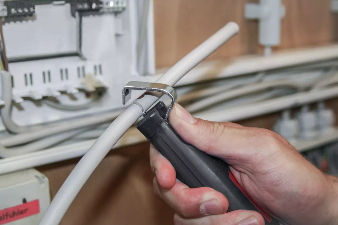 A person using a cable stripping tool on a white cable