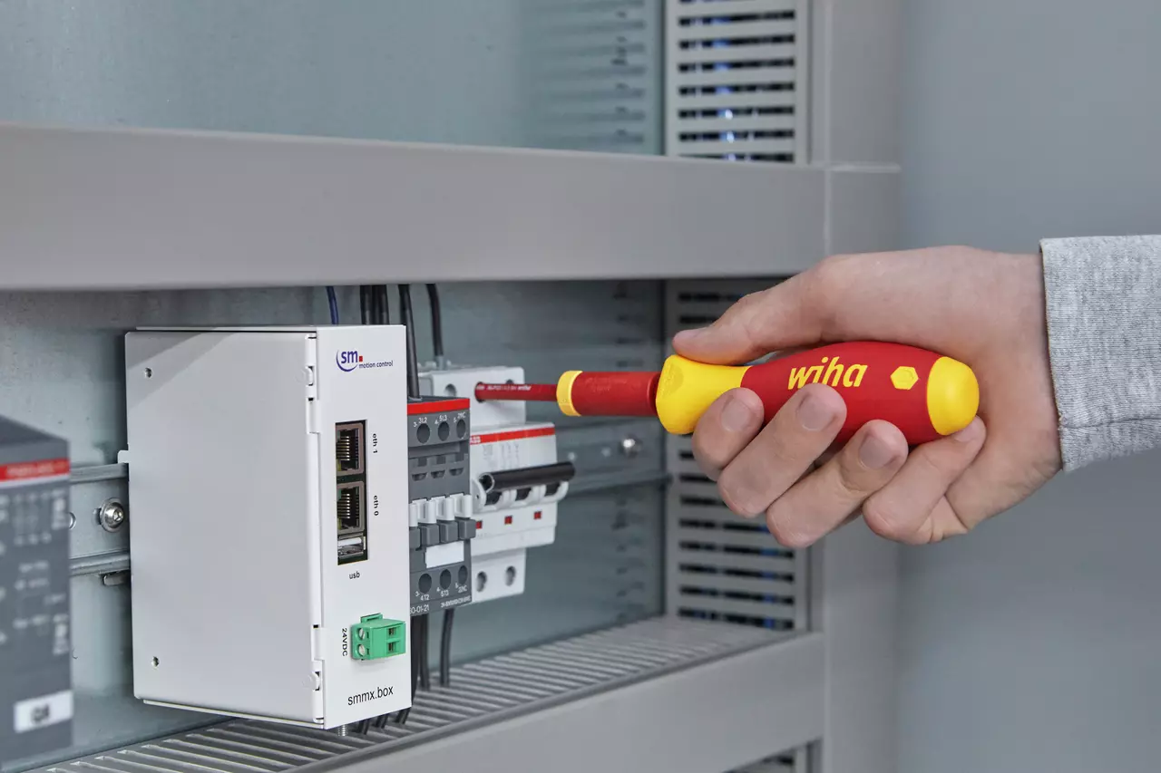 Hand using an electric screwdriver to adjust a component in an electrical panel.