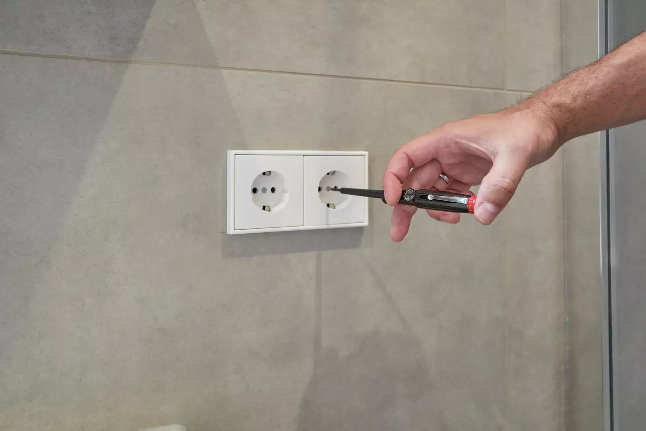 Hand using voltage tester on wall socket