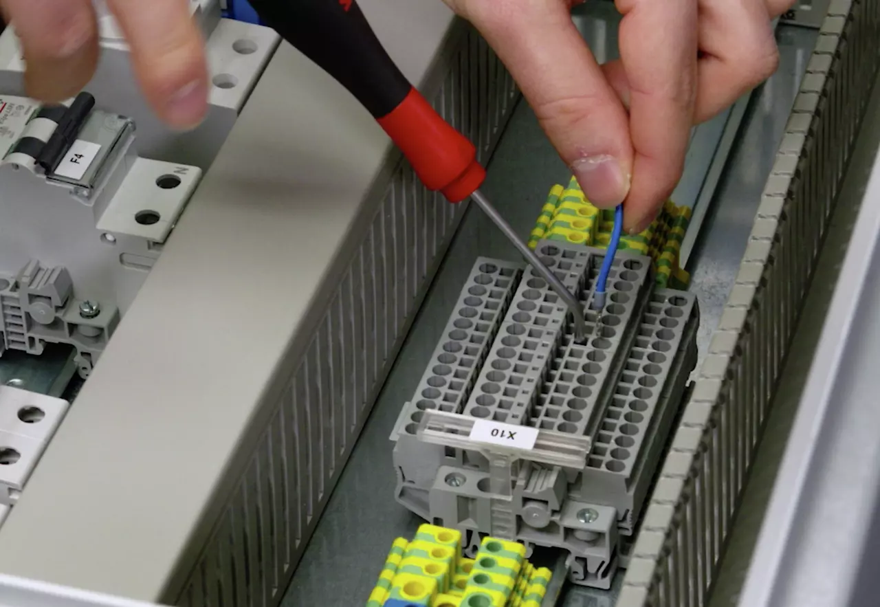 A person using a screwdriver to connect a blue wire to a terminal block in an electrical panel.