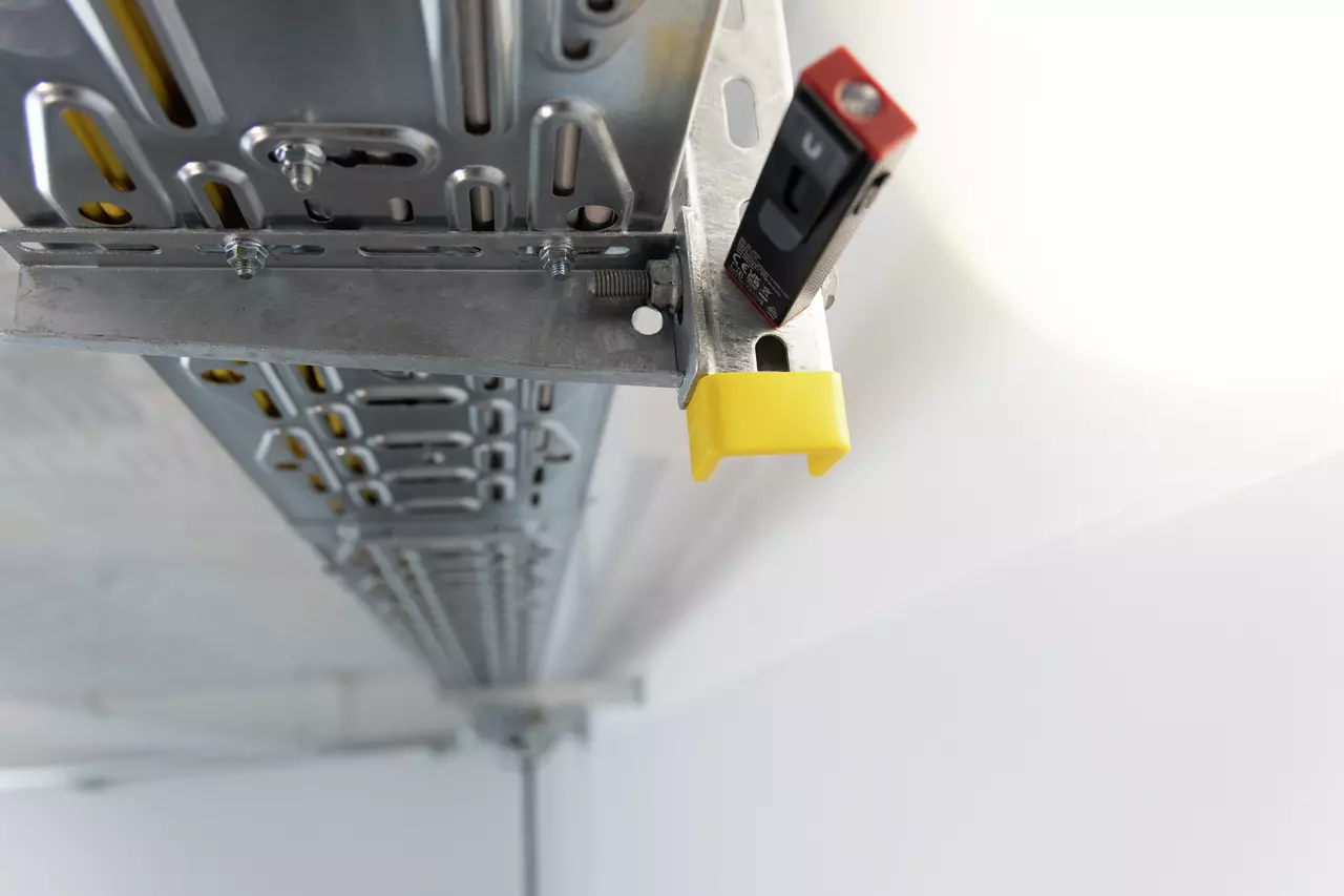 A metal cable tray with a yellow end cap and a small device attached.