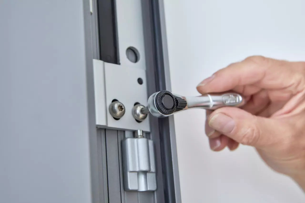 A hand uses a ratchet wrench on a metal surface with screws.