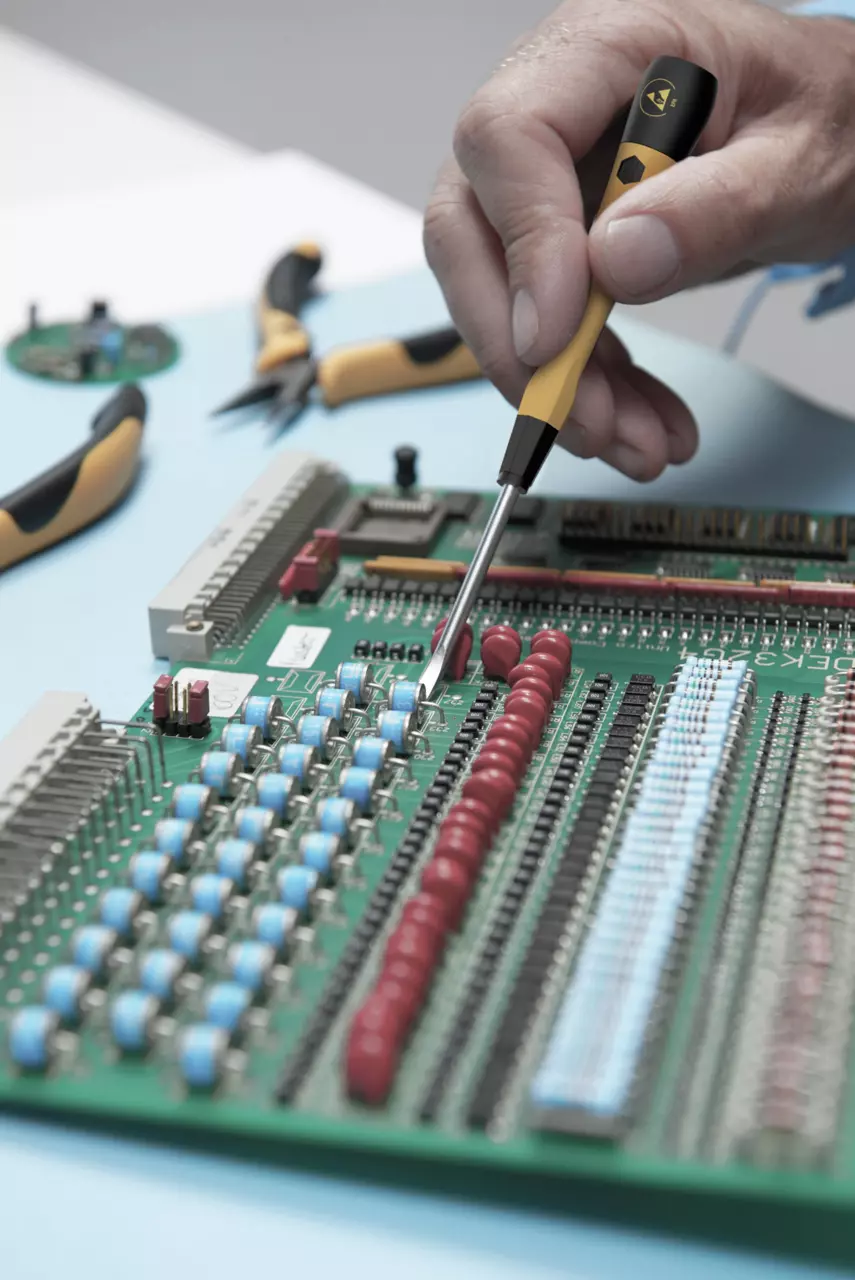 Hand holding precision screwdriver on a circuit board