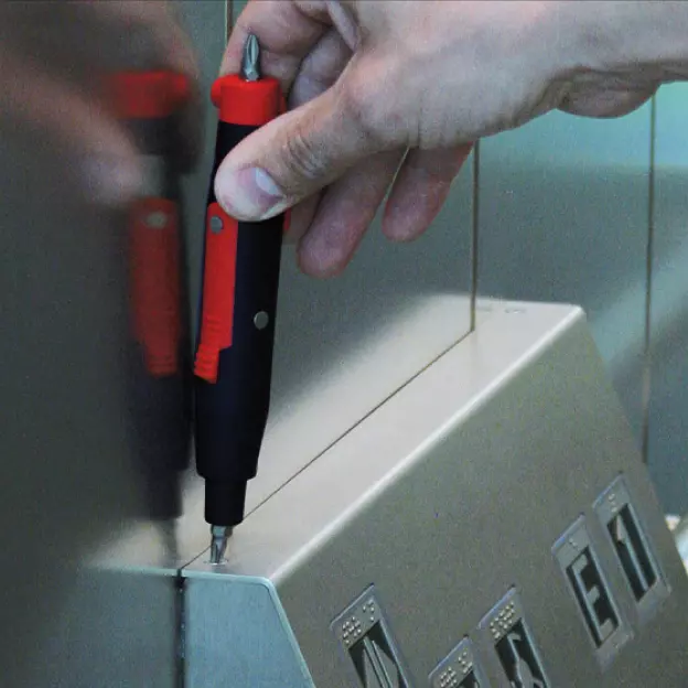 A person using an electric screwdriver on an elevator control panel.