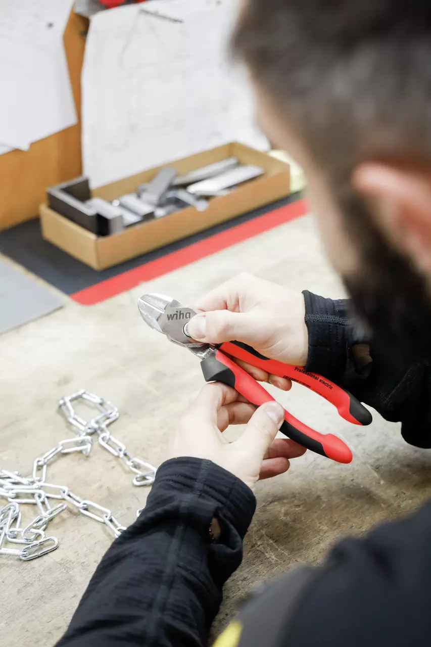 Person using red side cutter pliers on a metal chain on a table.